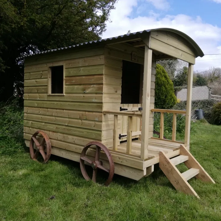 A wooden house with wheels and stairs is sitting in the grass.
