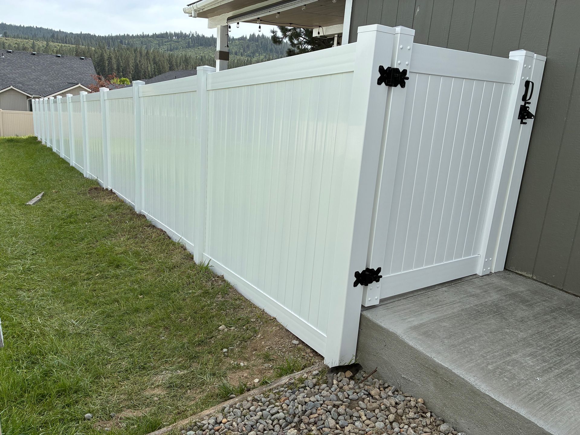 White vinyl fence and gate beside a gray house, bordering a grassy yard and concrete step.