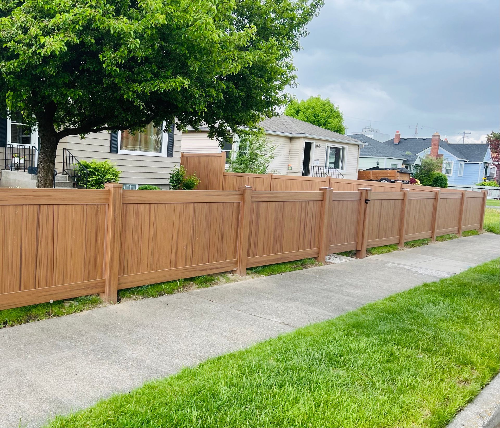 Wooden fence beside a sidewalk and green lawn in a suburban yard.