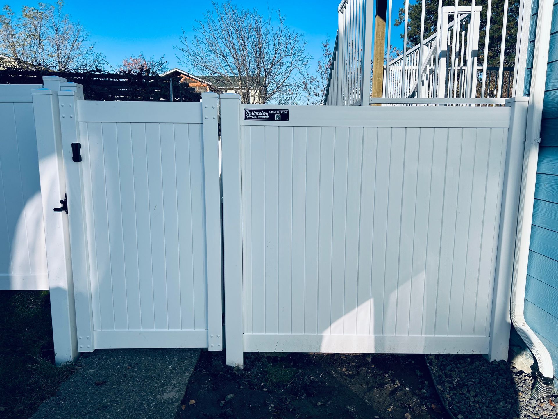 White vinyl fence and gate with a small sign, viewed in bright daylight.