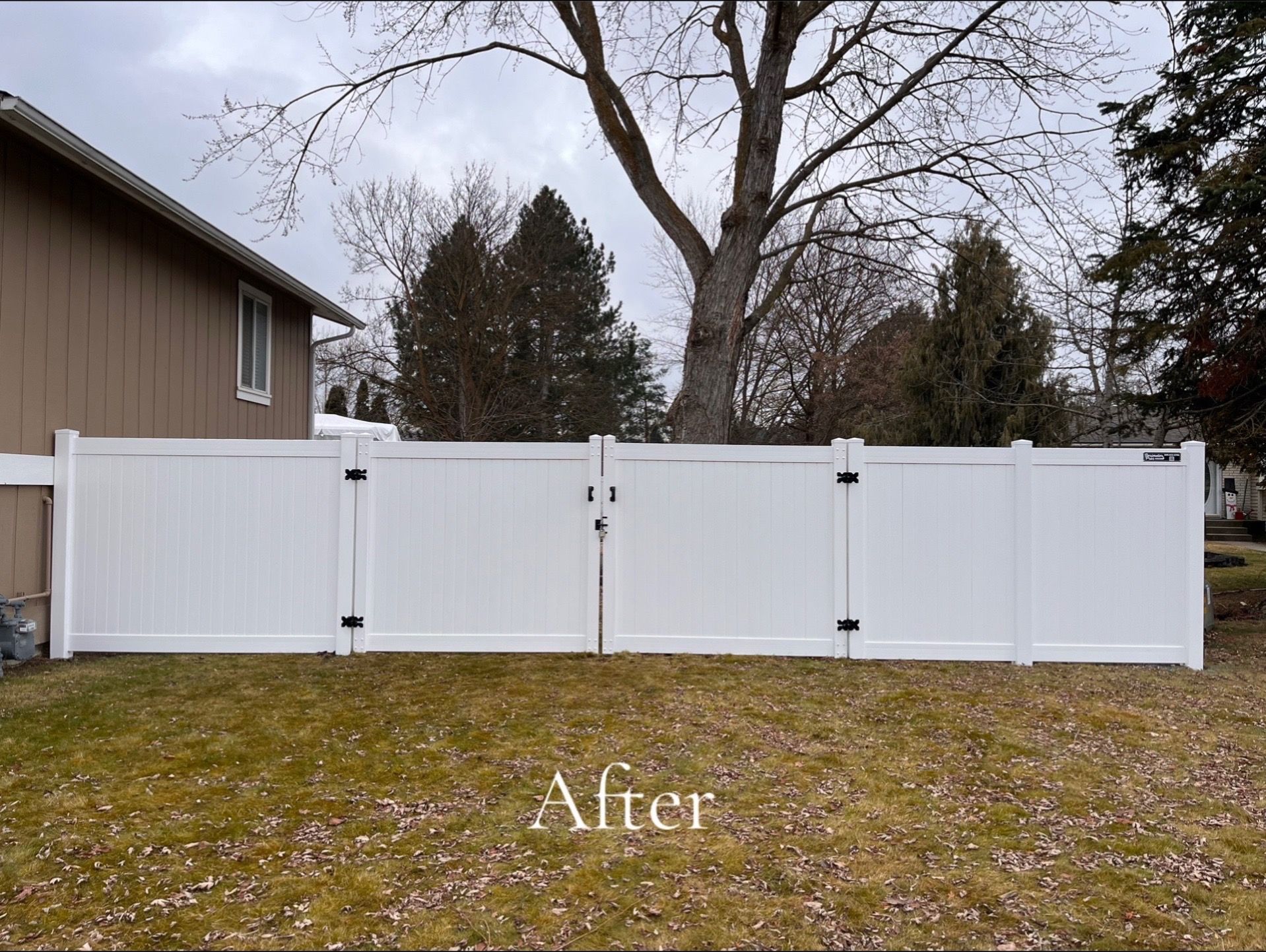 White vinyl fence panels installed across a backyard, with a house on the left and bare trees behind.