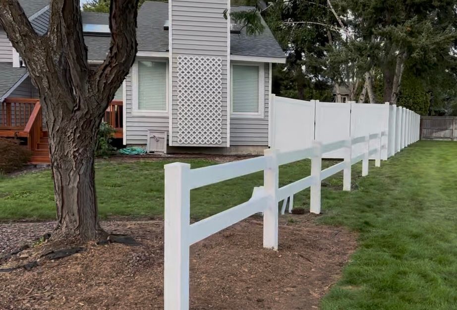 White fence along a grassy yard beside a house and tree