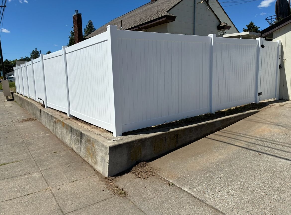 White vinyl fence around a corner lot beside a sidewalk and house under a clear blue sky