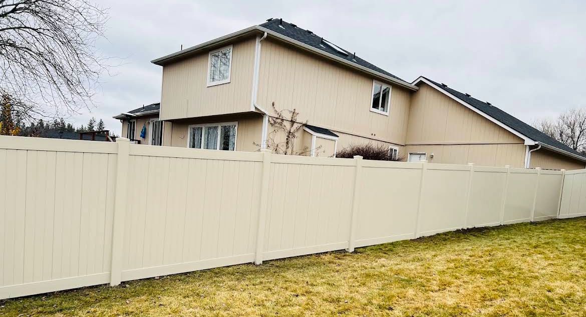 Beige house behind a cream fence on a grassy lawn under an overcast sky