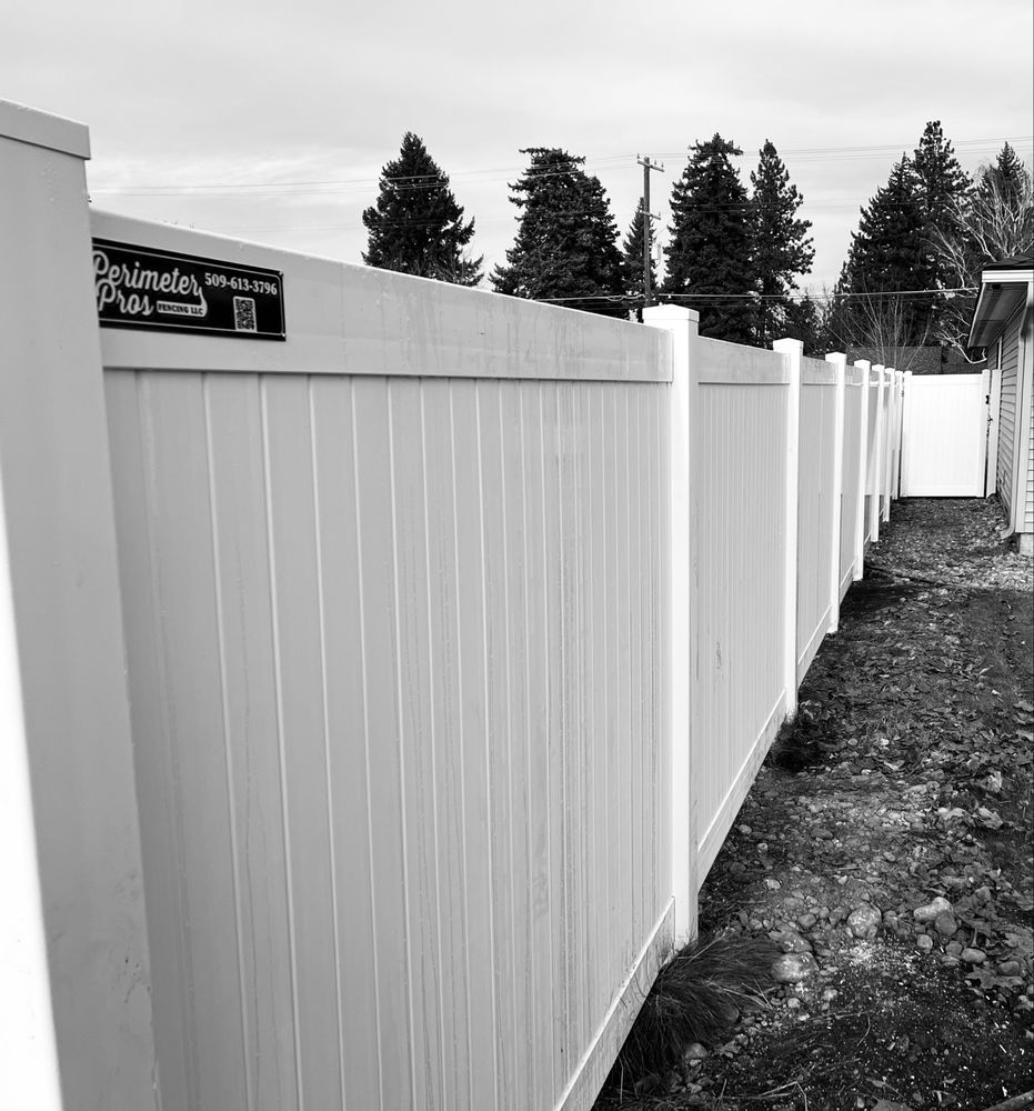 A white vinyl fence running along a narrow dirt path beside trees and a cloudy sky.