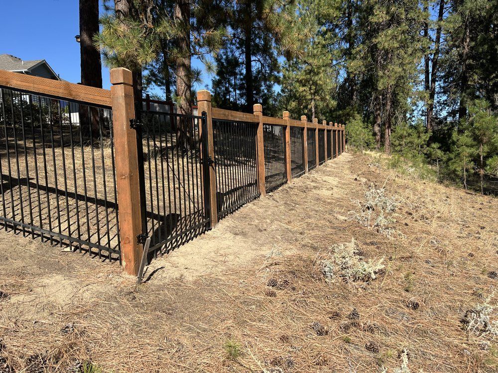 Wooden and black metal fence along a dry, wooded hillside path