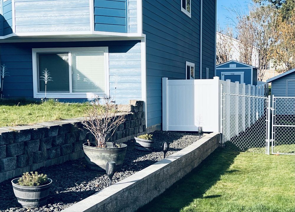 Blue house side yard with raised retaining wall, white fence, and grass lawn