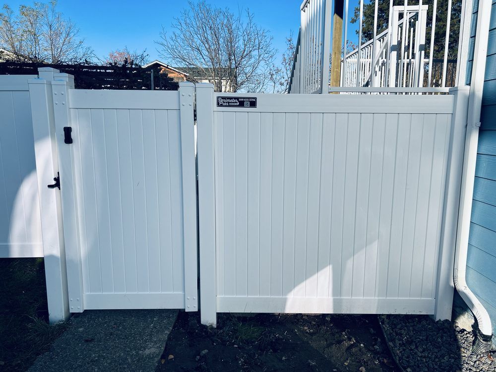 White vinyl gate and fence beside a house, with a side door and winter trees in the background