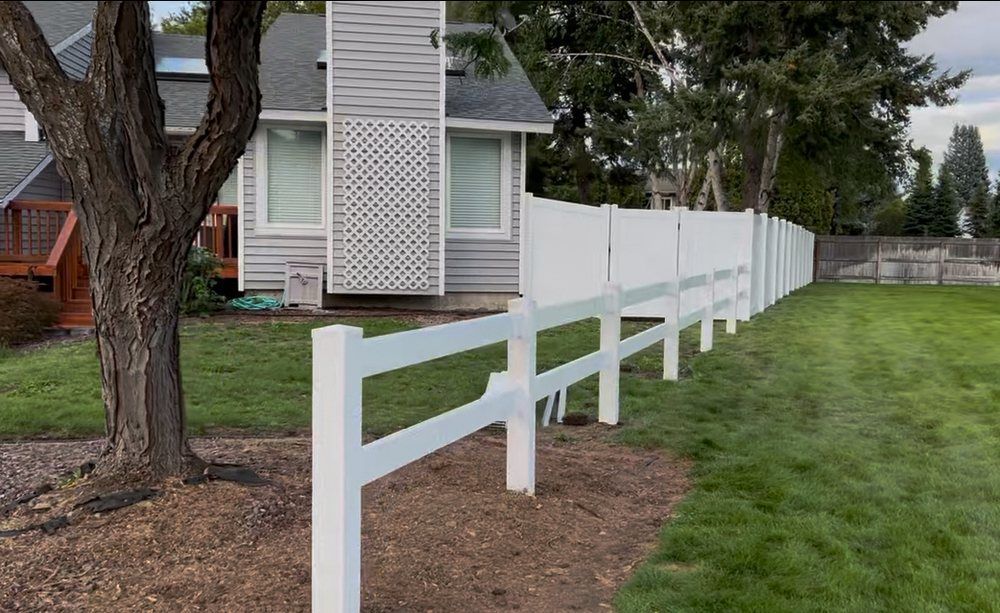 White fence running along a suburban yard beside a house and tree