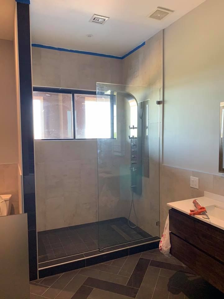 A modern bathroom with a glass shower enclosure and dark tiled floor.