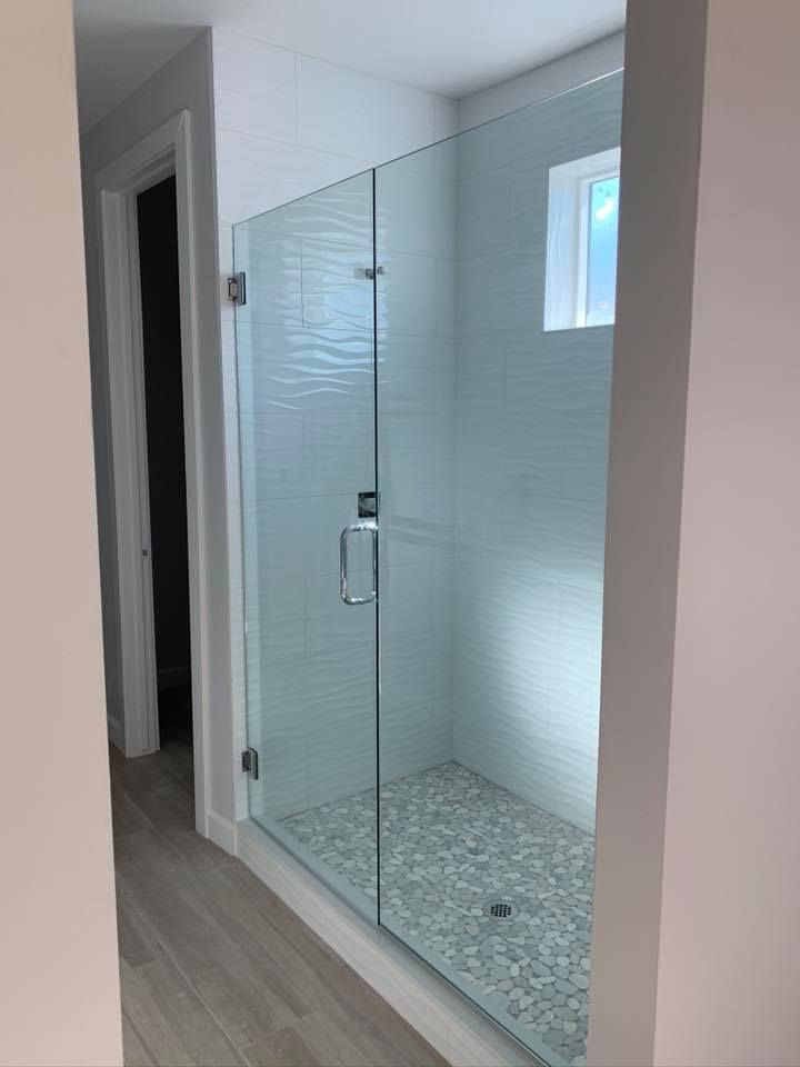 Glass shower enclosure with pebble floor and white wave-patterned tile walls; doorway to the left.