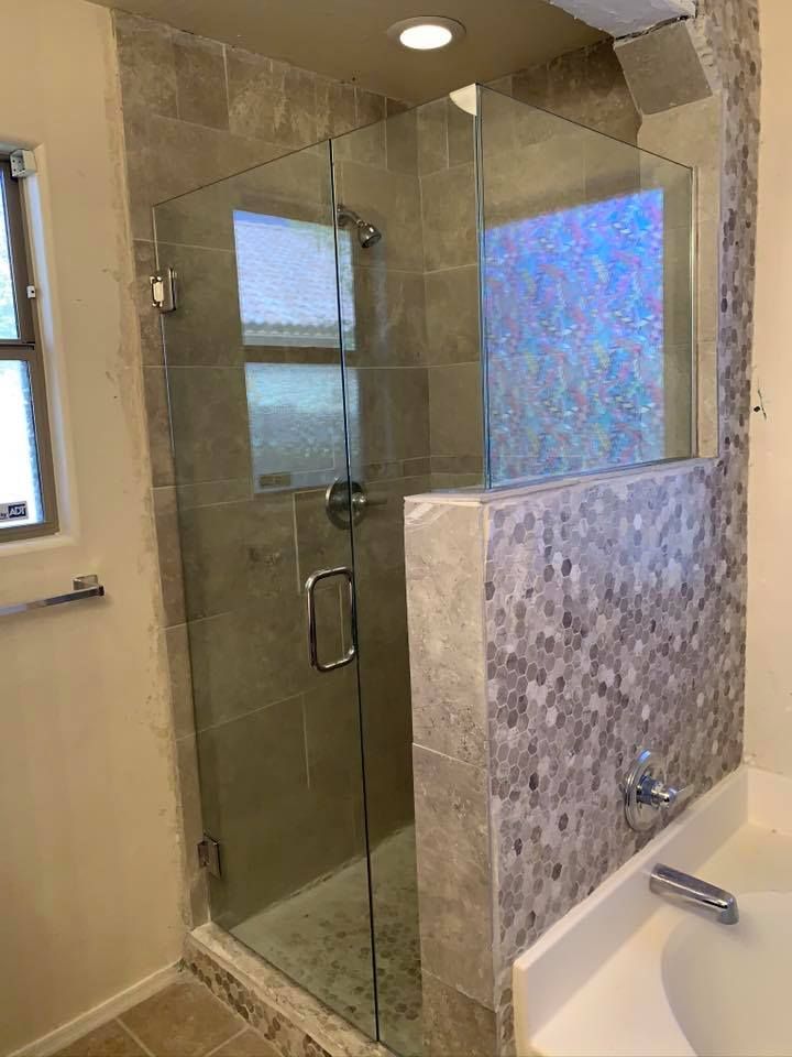Glass shower enclosure in a bathroom, featuring a tiled wall and a window.