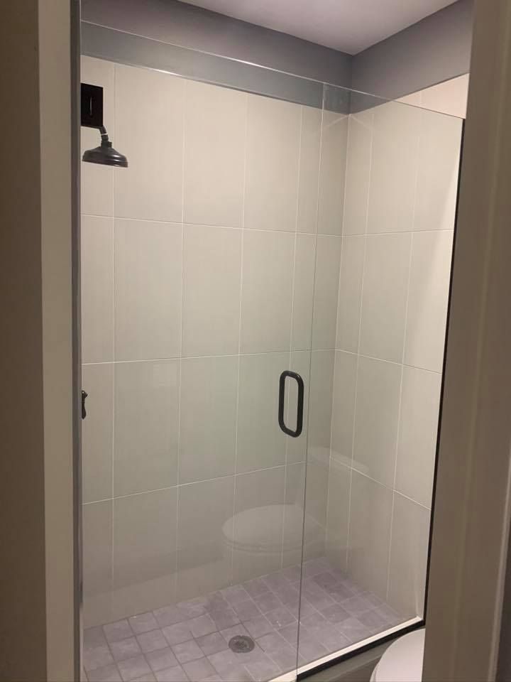 A clear glass shower stall with gray tiles, a dark handle, and a black showerhead.