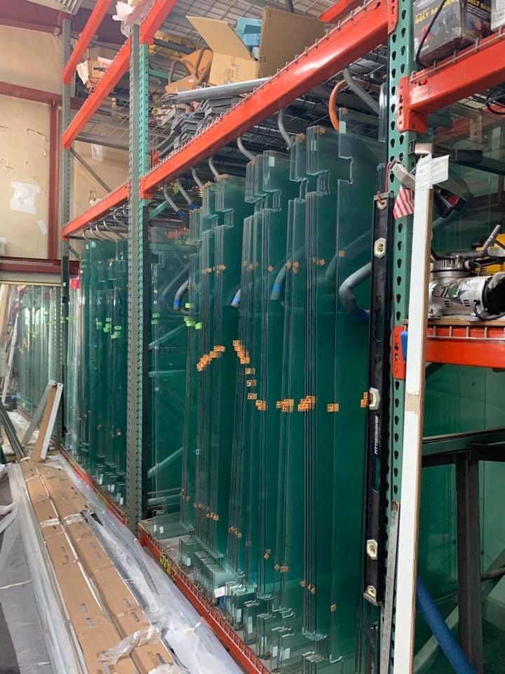 Shelving unit filled with multiple large, green glass panels, likely for construction, in a warehouse setting.