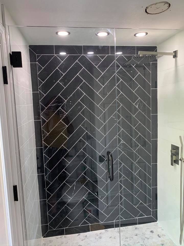 Black herringbone tile shower with glass door and black hardware.