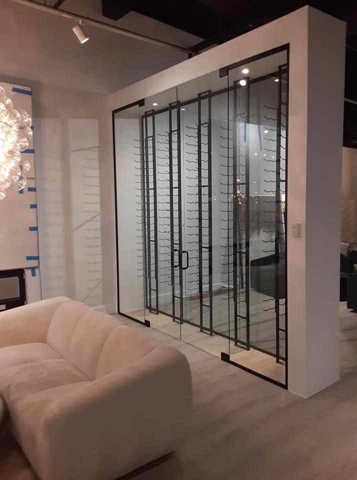 Modern wine cellar with glass doors and black metal accents, next to a white sofa.