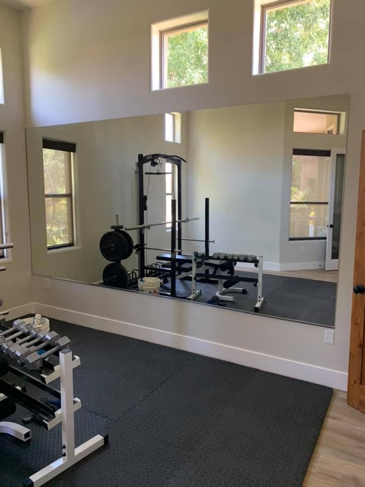 Home gym with mirror, weights, and weight rack on black rubber floor.