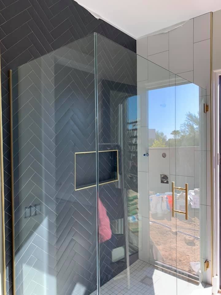 Shower with glass doors, dark gray herringbone tiles, gold accents, and white tiles.