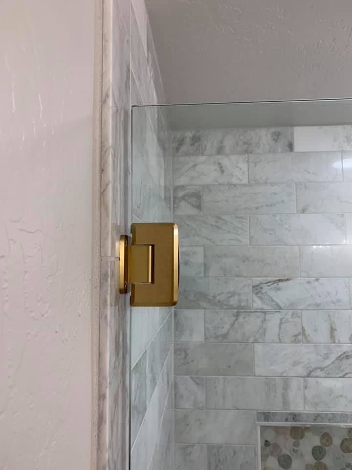 Gold shower door hinge attached to marble tiles and glass.