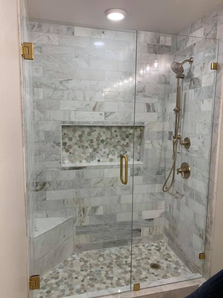 A luxurious glass shower with marble walls and a stone pebble floor. Gold hardware accents the fixtures.