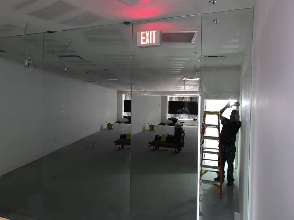 Man on ladder installing mirrored wall panel in an open room with an