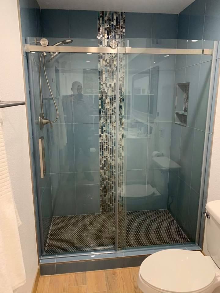 Shower stall with glass doors and blue tile. A person's reflection is visible.