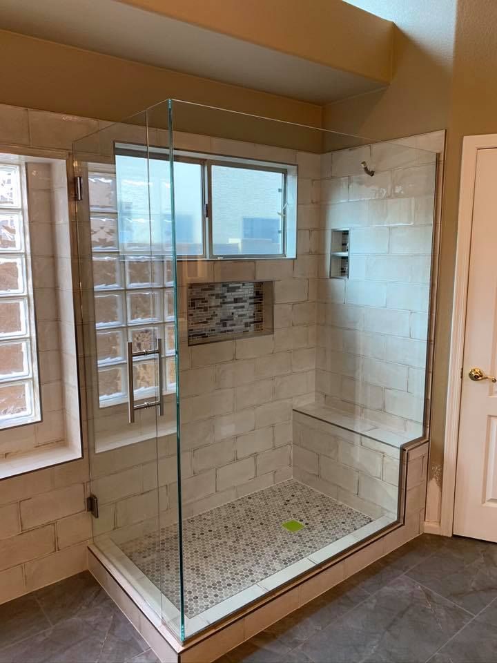 Modern shower with glass door, tiled walls, bench, and small window, in a bathroom.