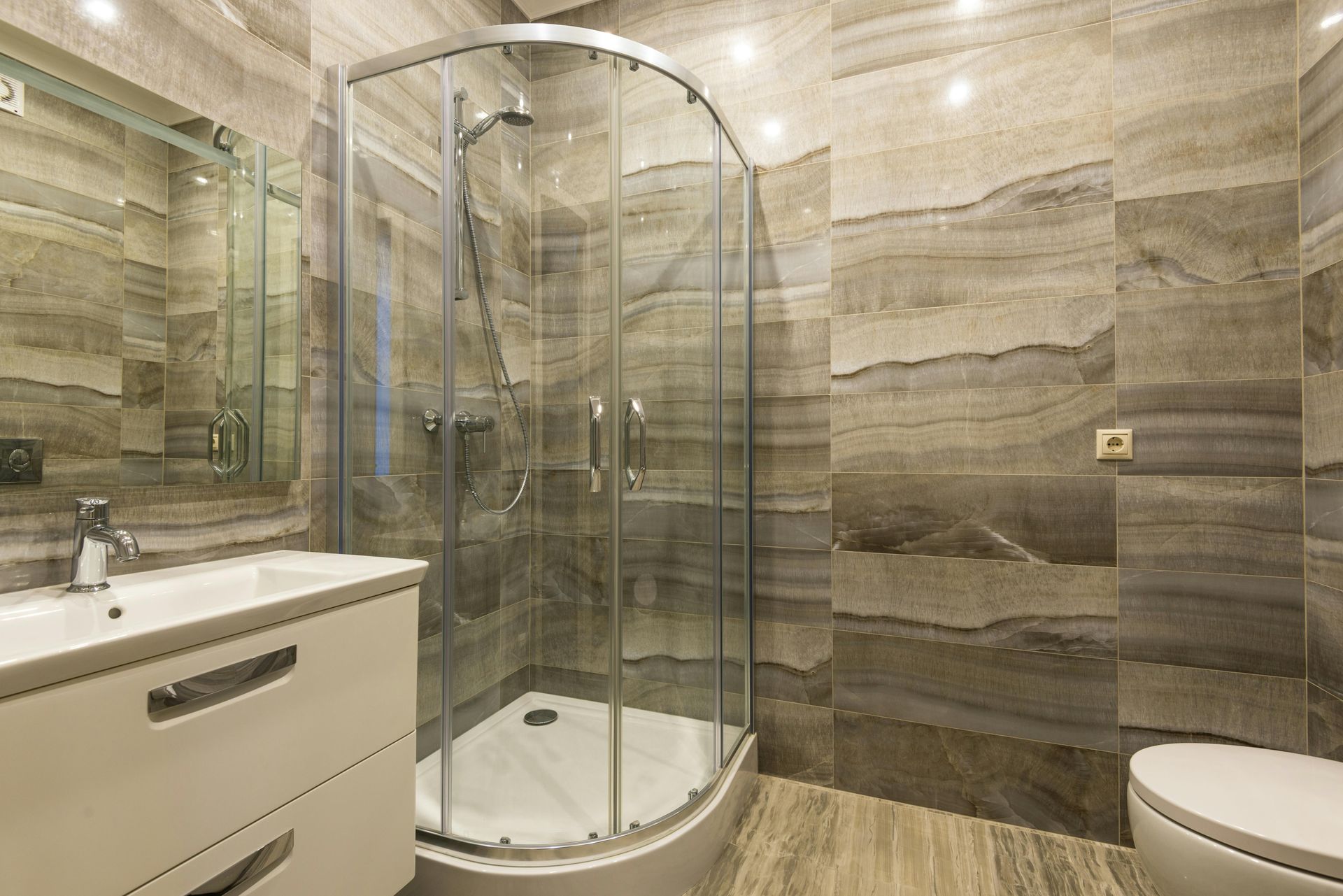 Modern bathroom featuring a corner shower enclosure, vanity sink, and textured brown stone-look wall tiles.