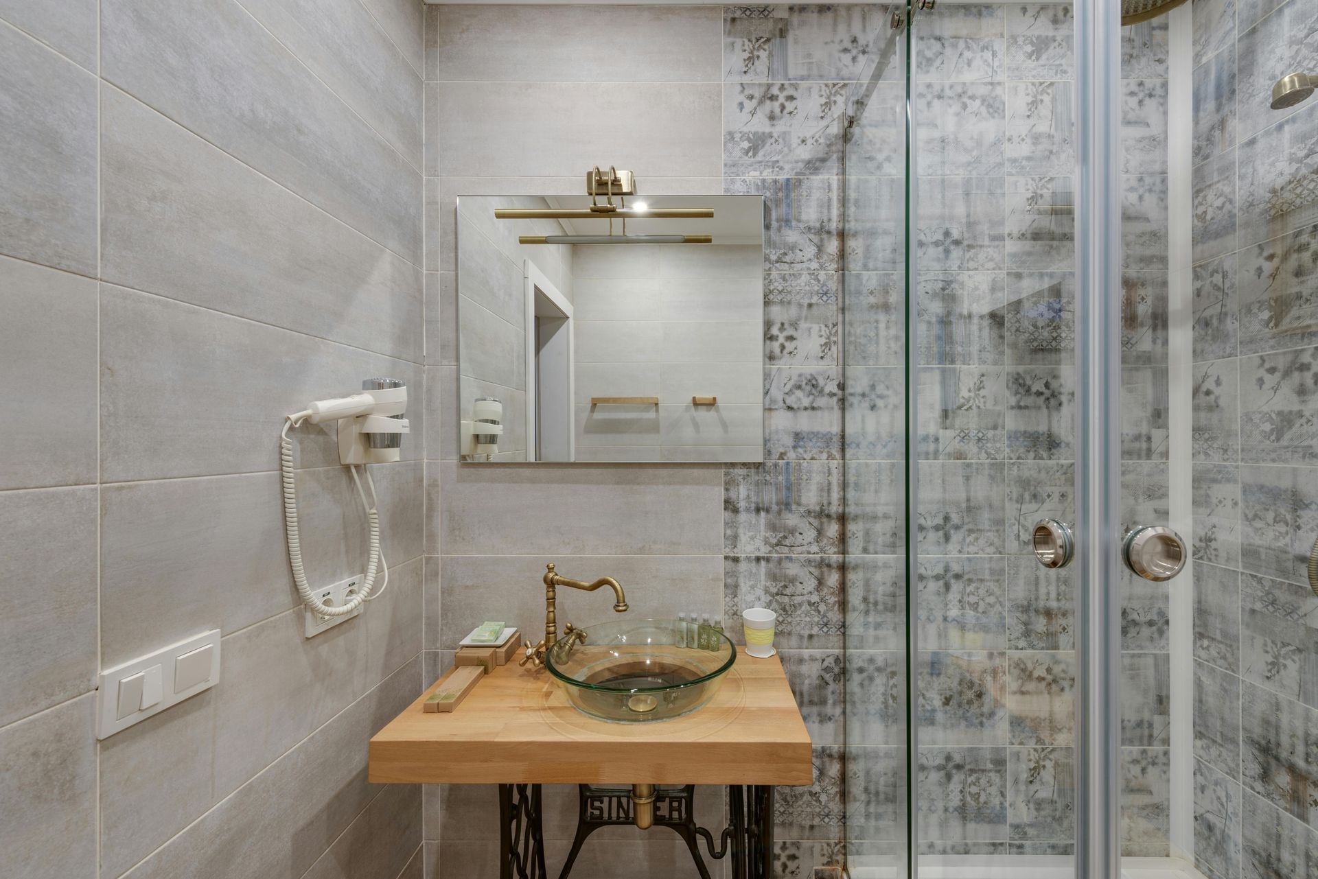 Small bathroom with glass shower, mirror, sink, and gold fixtures on a wood vanity.