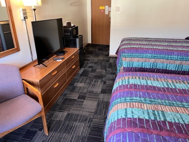 A motel room with a bed, dresser, television and refrigerator.