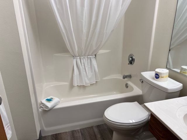 A bathroom with a tub, toilet, mirror and shower curtain.