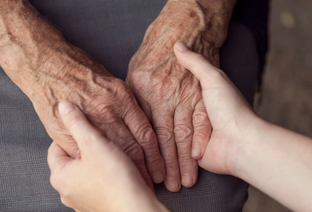 Close-up of two pairs of hands, one elderly and one younger, gently holding each other