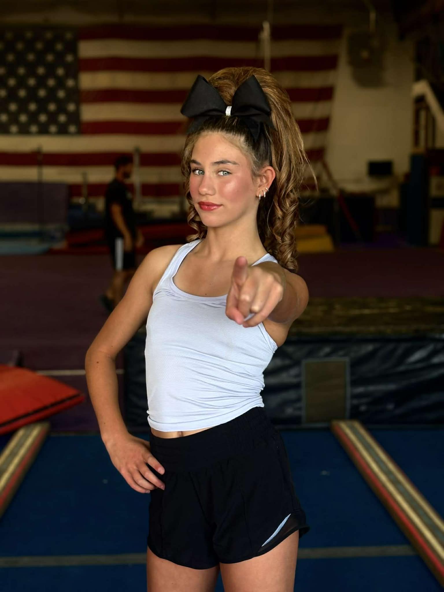Cheerleaders in blue and white uniforms pose with arms outstretched on a blue mat in a gym.
