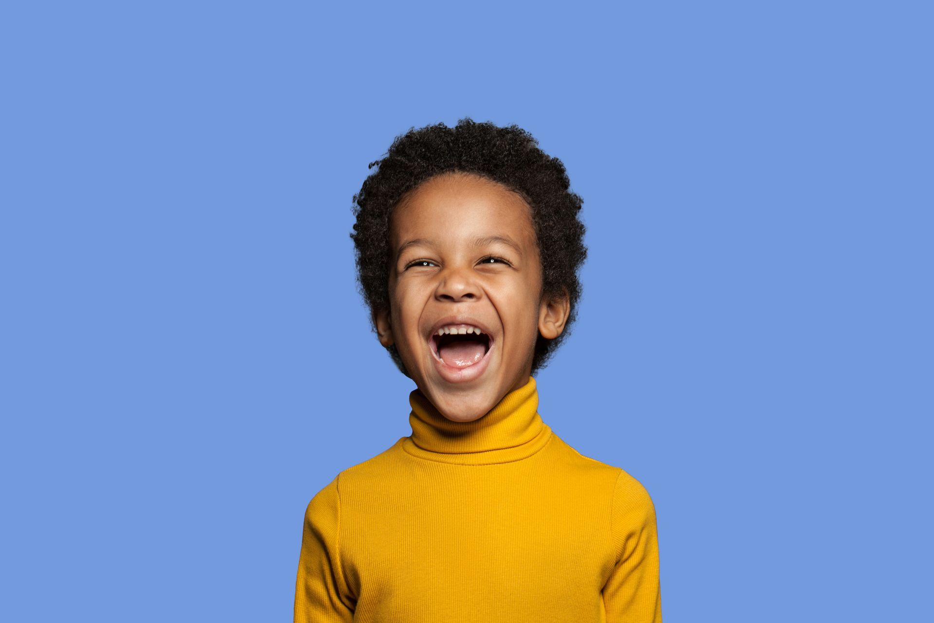Smiling Black child with curly hair wearing a yellow turtleneck, set against a blue background.