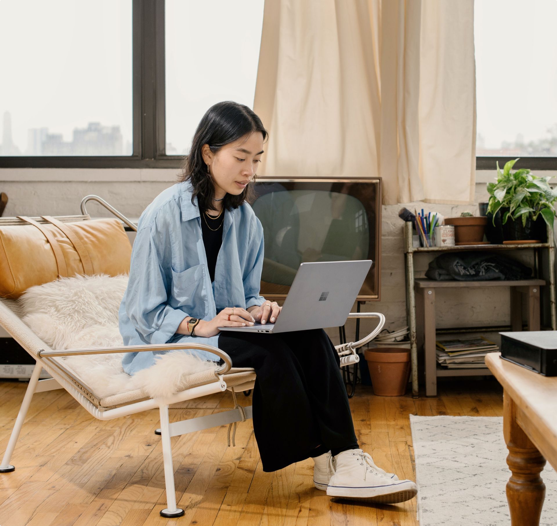 Woman in blue shirt typing on a laptop in a well-lit living room.