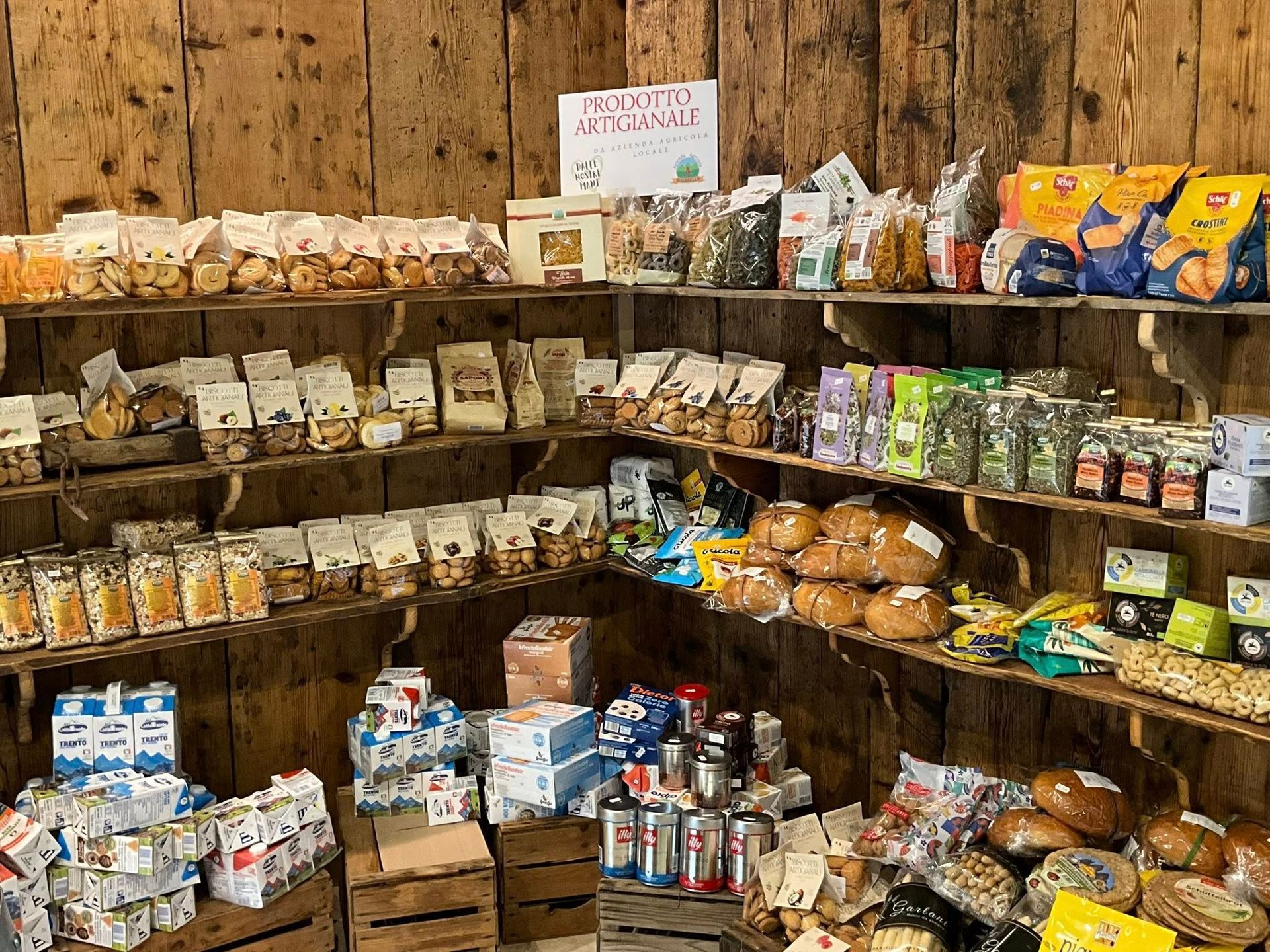 Scaffali pieni di snack e bevande confezionati assortiti, in un'esposizione rustica da negozio di alimentari o dispensa.