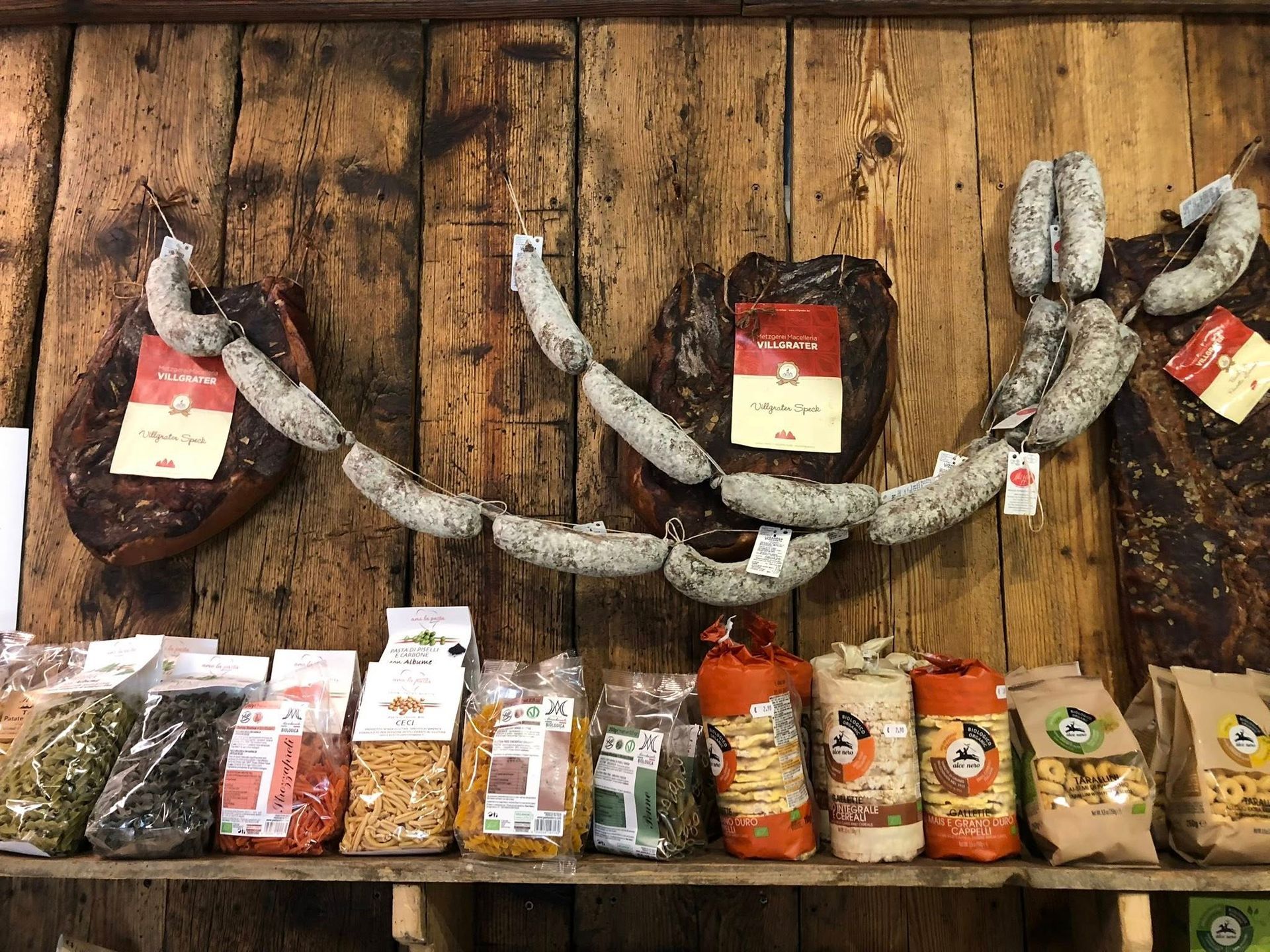Carne e salsicce confezionate esposte su scaffali contro una parete di legno rustica.