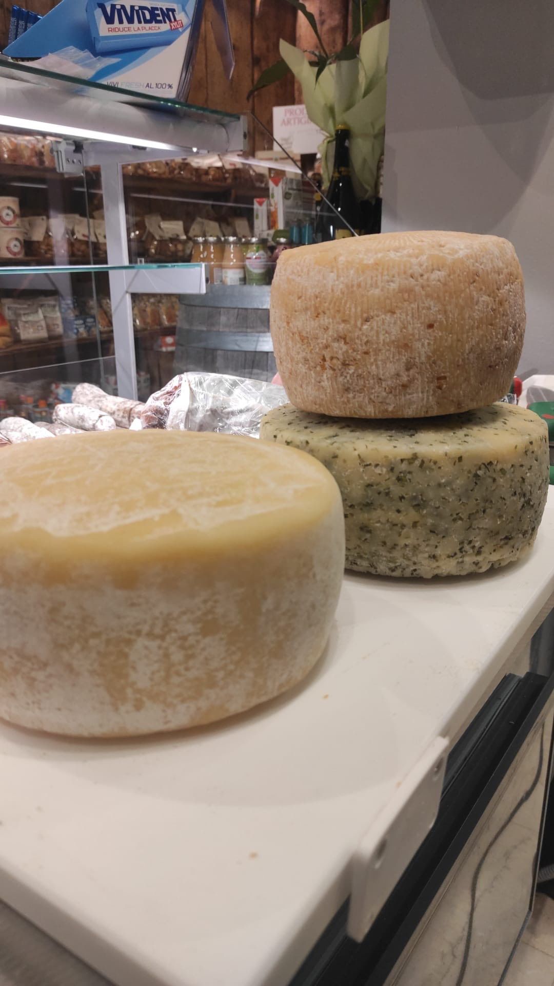 Formaggi rotondi impilati in una vetrina gastronomica, con una forma chiara davanti e due impilate dietro.