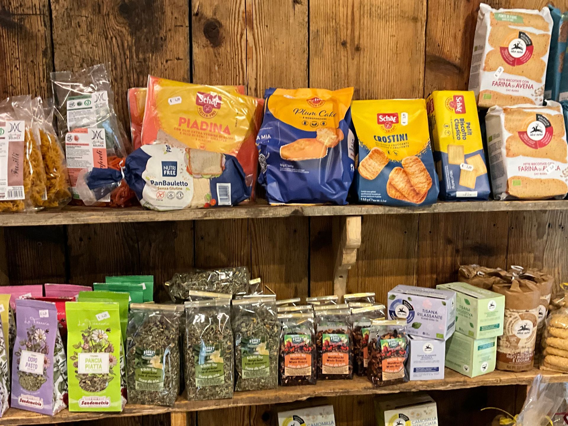 In un negozio rustico, un assortimento di snack confezionati e prodotti secchi sono disposti su scaffali di legno.