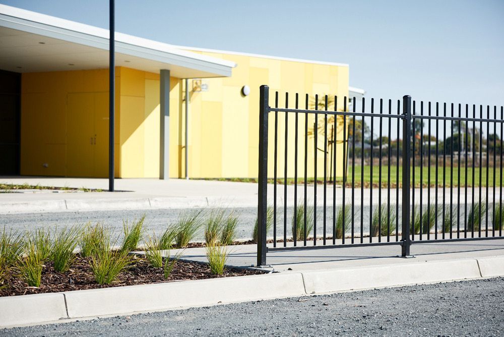 A Yellow Modern Building Sits Behind a Dark Metal Picket Fence — Quarrell Civil Construction In Congupna, VIC