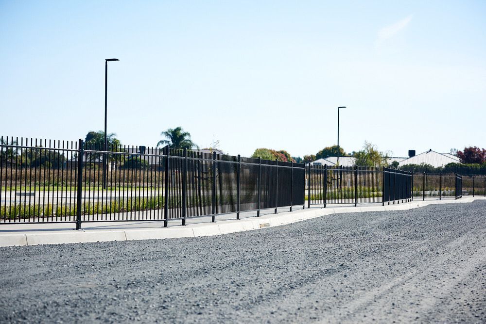 A Black Metal Fence Runs Along a Gravel Path — Quarrell Civil Construction In Congupna, VIC