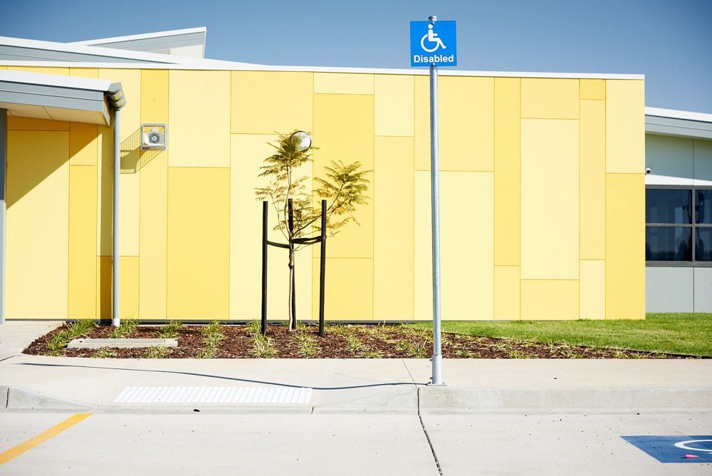 A Blue Wheelchair Accessible Parking Sign Stands in Front of a Modern Building — Quarrell Civil Construction In Congupna, VIC