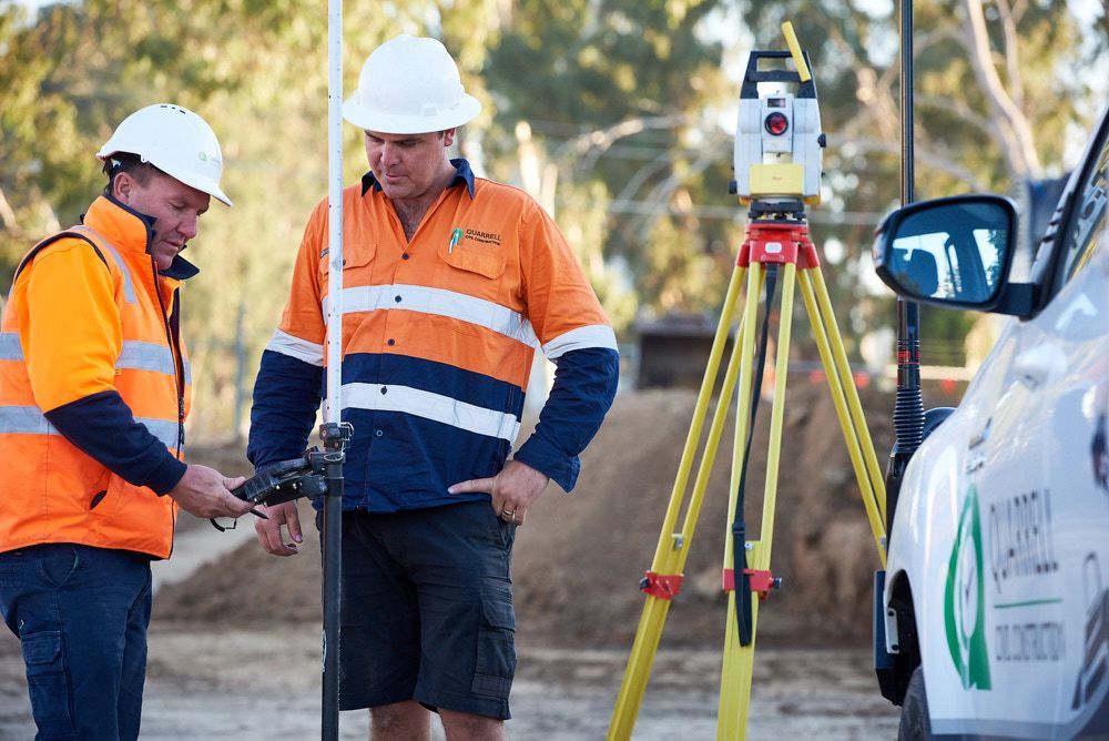 Two Workers In Safety Vests And Hard Hats Surveying Equipment Outdoors — Quarrell Civil Construction In Congupna, VIC