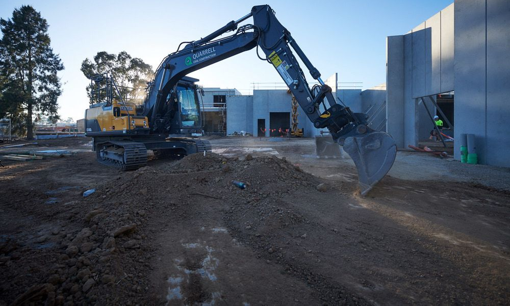 Excavator at a construction site, scooping dirt on a sunny day. — Quarrell Civil Construction In Congupna, VIC