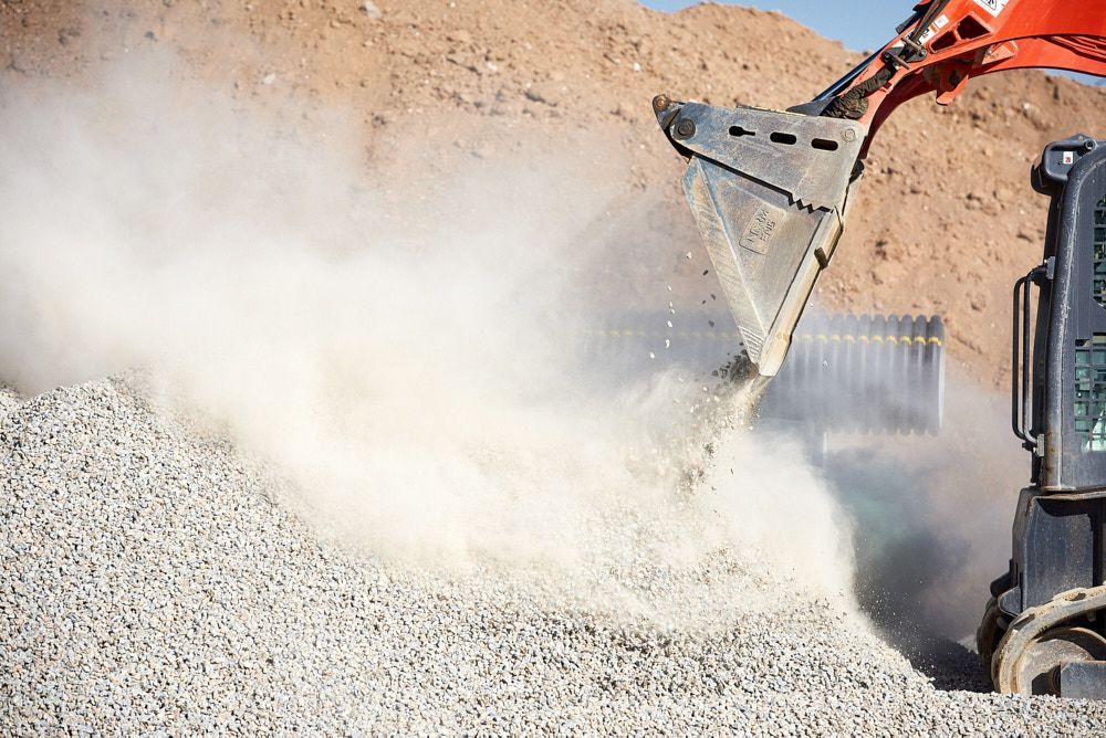 A Heavy Machinery Bucket Drops Gravel Onto a Pile — Quarrell Civil Construction In Congupna, VIC