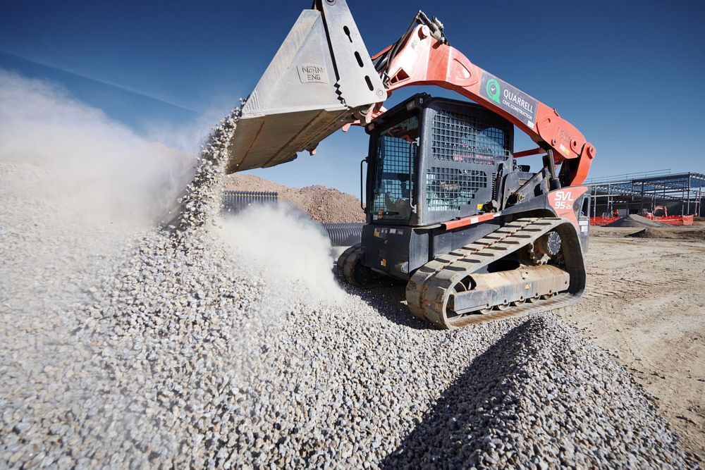 An Orange Compact Track Loader Dumps a Bucket of Gravel — Quarrell Civil Construction In Congupna, VIC