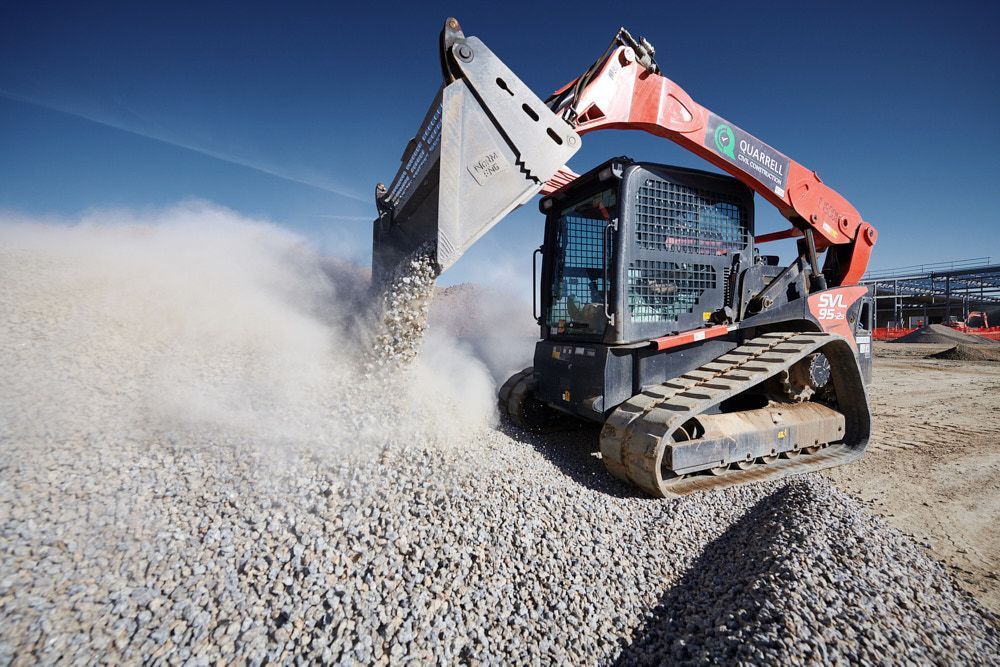 An Orange Tracked Skid Steer Loader Dumping a Bucket of Gravel — Quarrell Civil Construction In Congupna, VIC