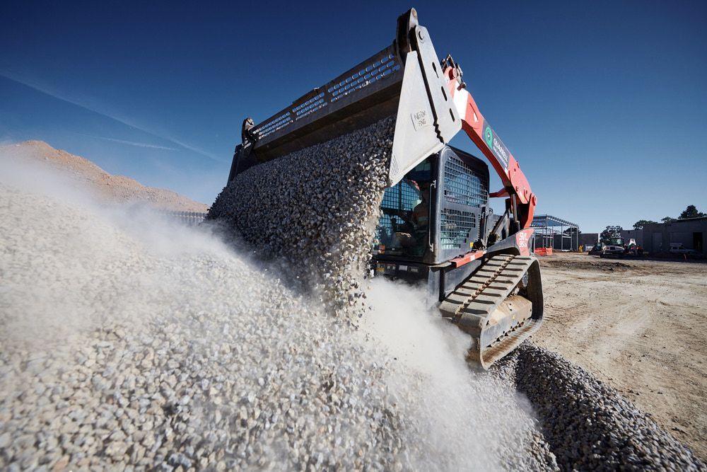 A Construction Skid Steer Loader Dumps a Load of White Gravel — Quarrell Civil Construction In Congupna, VIC