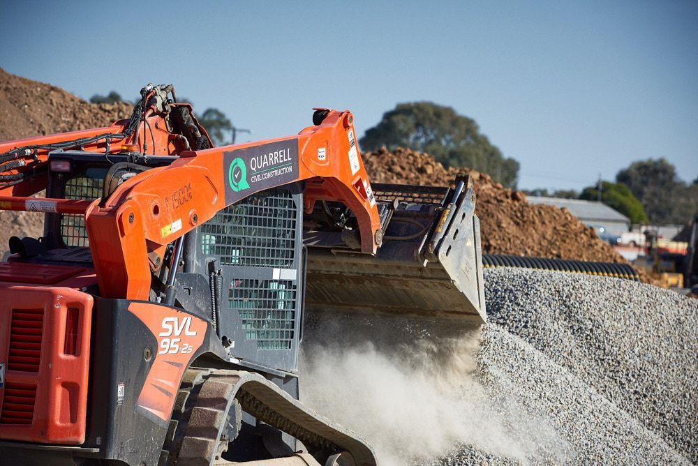Orange Kubota Skid Steer Loading Gravel At A Construction Site — Quarrell Civil Construction In Congupna, VIC