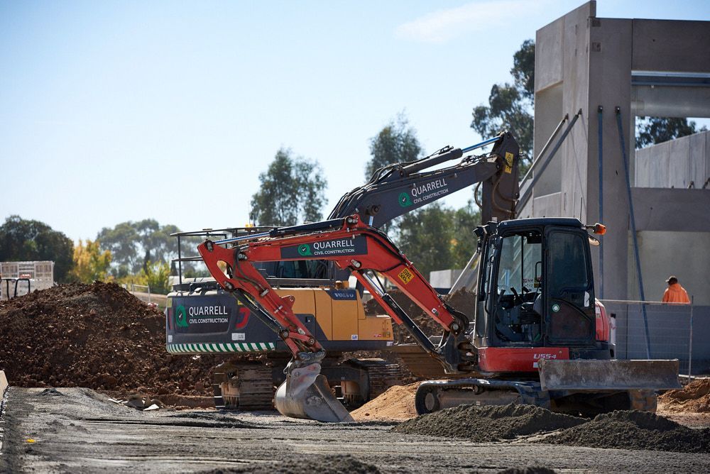 Construction site with excavators, a building, and dirt under a blue sky. — Quarrell Civil Construction In Congupna, VIC